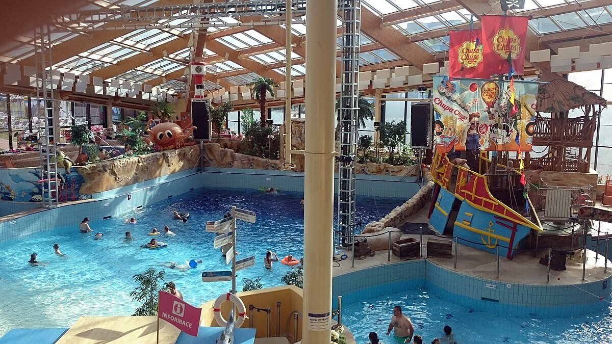 The indoor water park at Aquapalace Prague, with swimming pools and a pirate-ship play structure under a glazed roof.